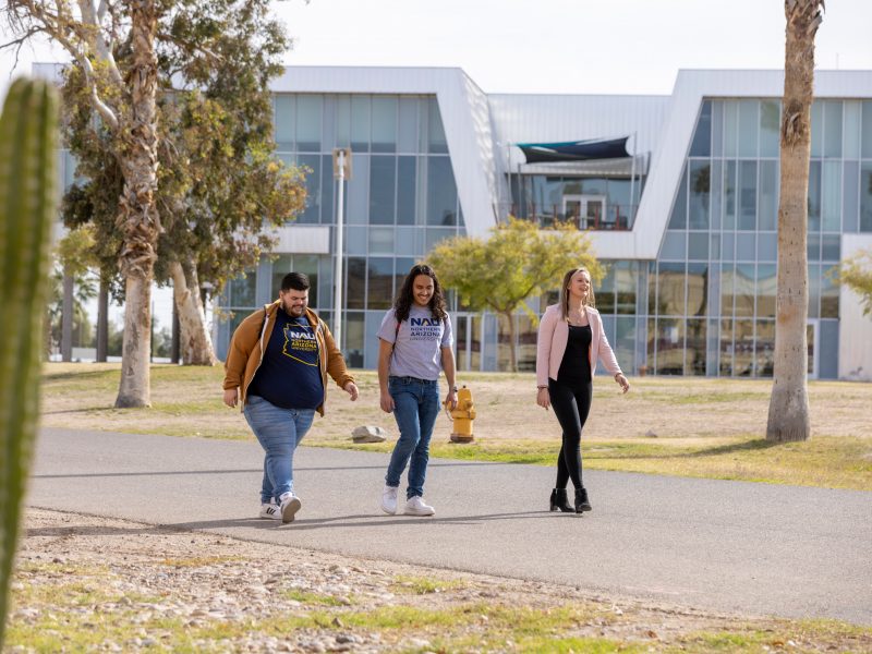 Three students walk and talk around the N A U Yuma campus.
