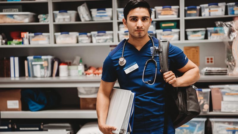 Nursing student with backpack and binder walking out of a classroom.