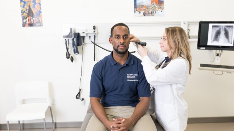 A person sitting on a exam table while a physician uses an otoscope.