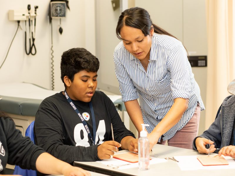 A student sitting on an exam table with two physician assistants.