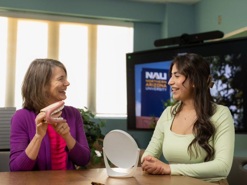 A professor and student sit at a table in front of a small mirror.