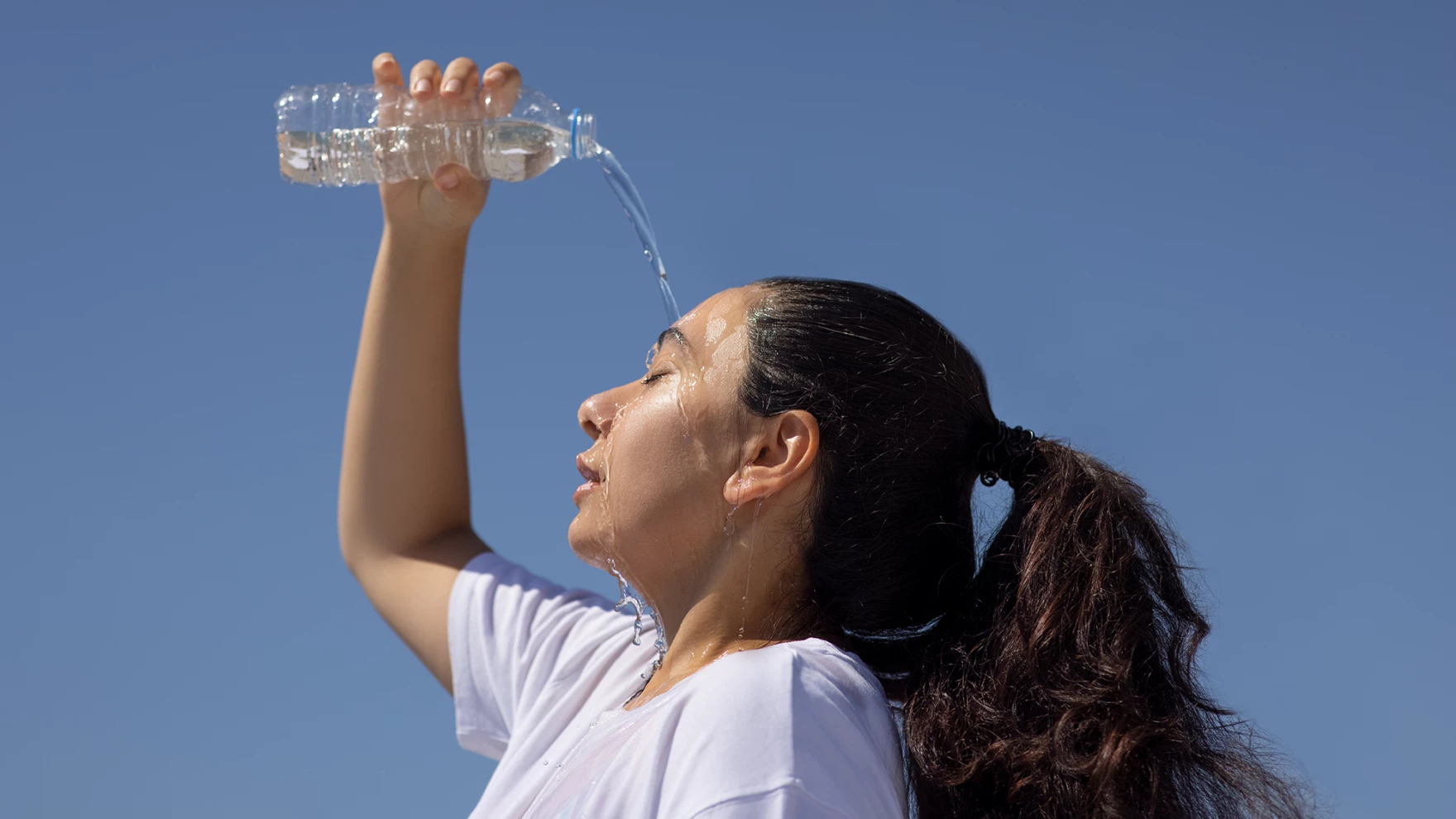A woman in the sun pouring water on her head to cool down.