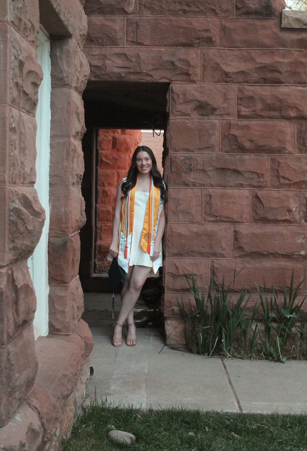 Cidney Roper in graduate regalia and a white dress next to Old Main.
