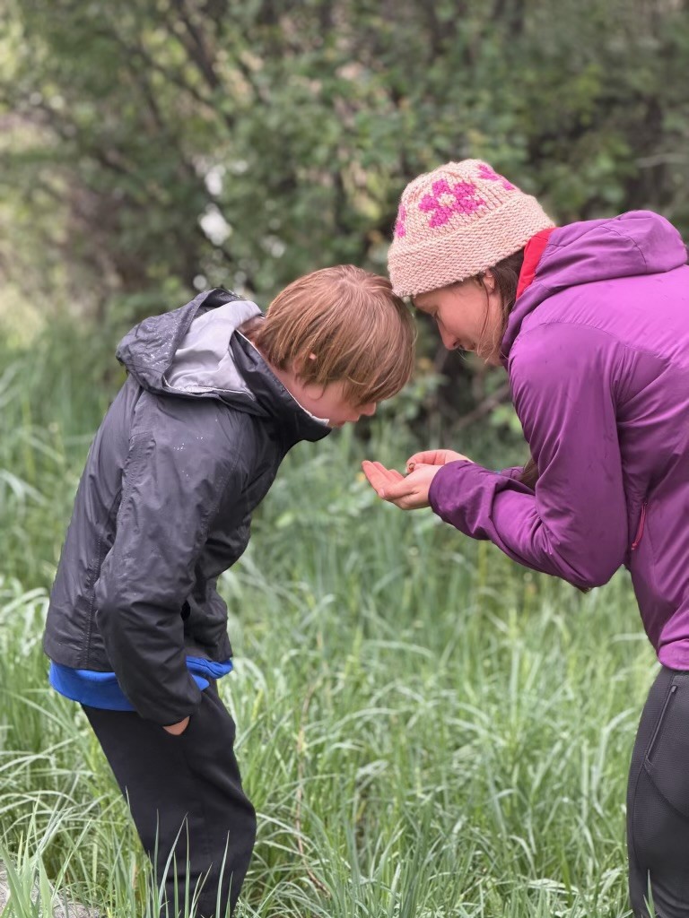Ella Welsh and a young OT client in a field looking at something she holds in her hand. 