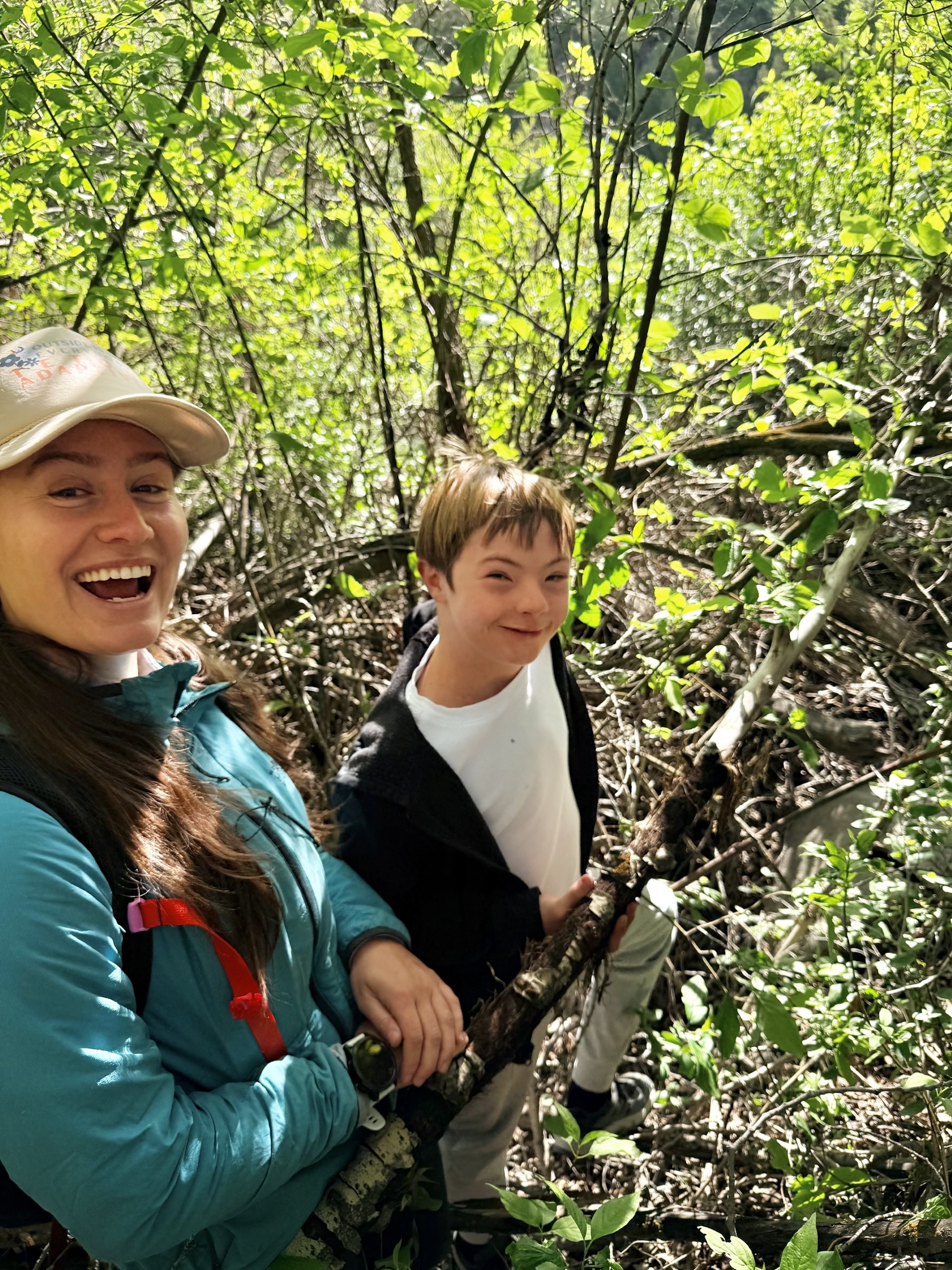 Ella Welsh and young OT client walking on a trail in the woods and smiling at the camera.