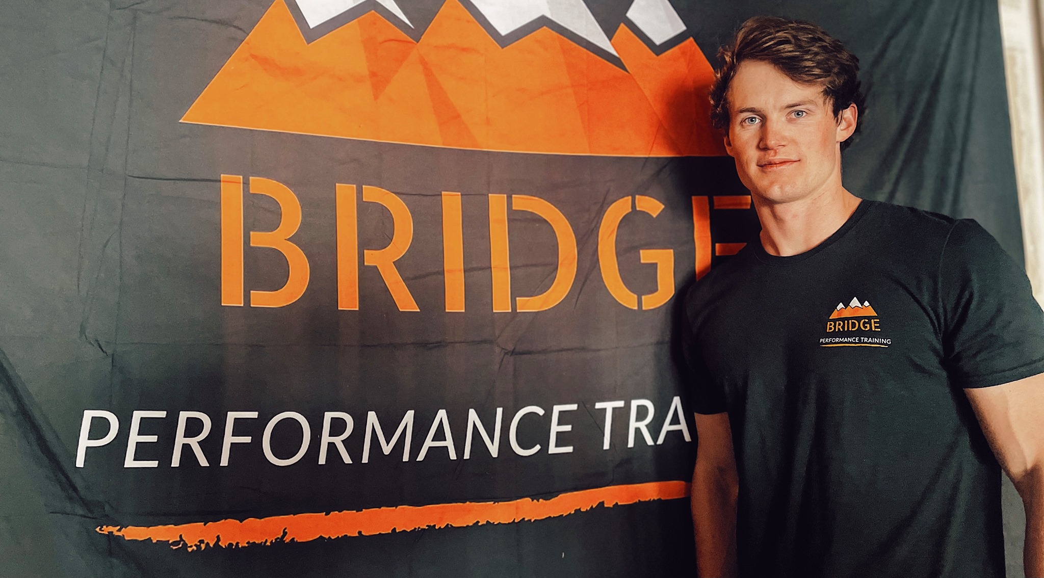 Briger Hershey posing in front of his gym's orange banner logo.