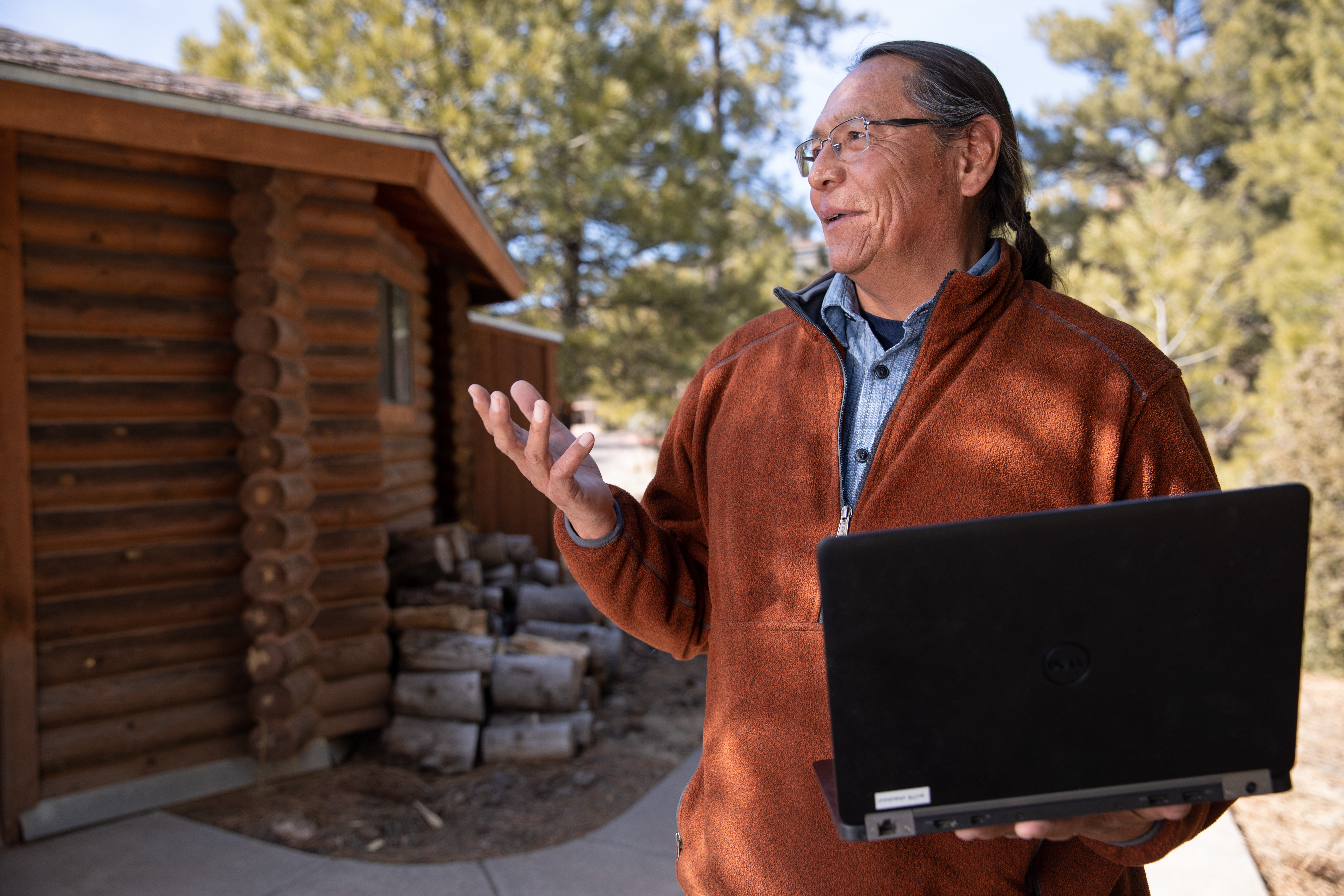 Faculty holding laptop outdoors.