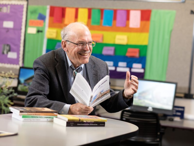 Jon Reyhner laughing in the distance while holding a book open.