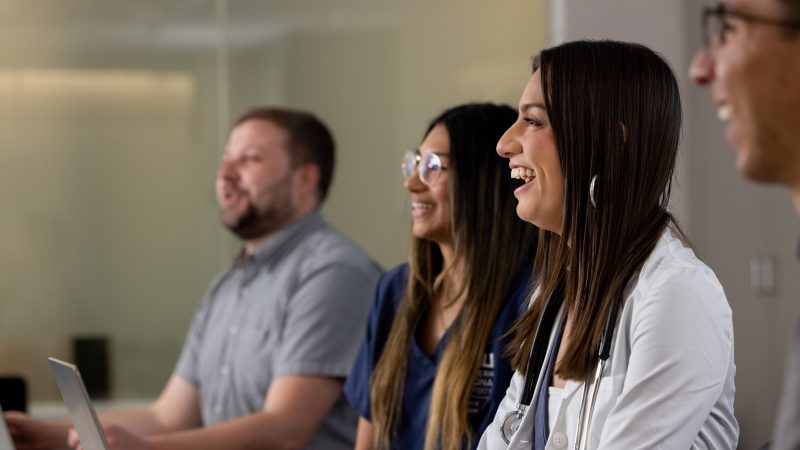Students and people apart of the health administration department laughing at something in the distance.