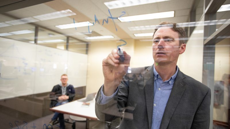 Faculty member writing on glass with a whiteboard marker.