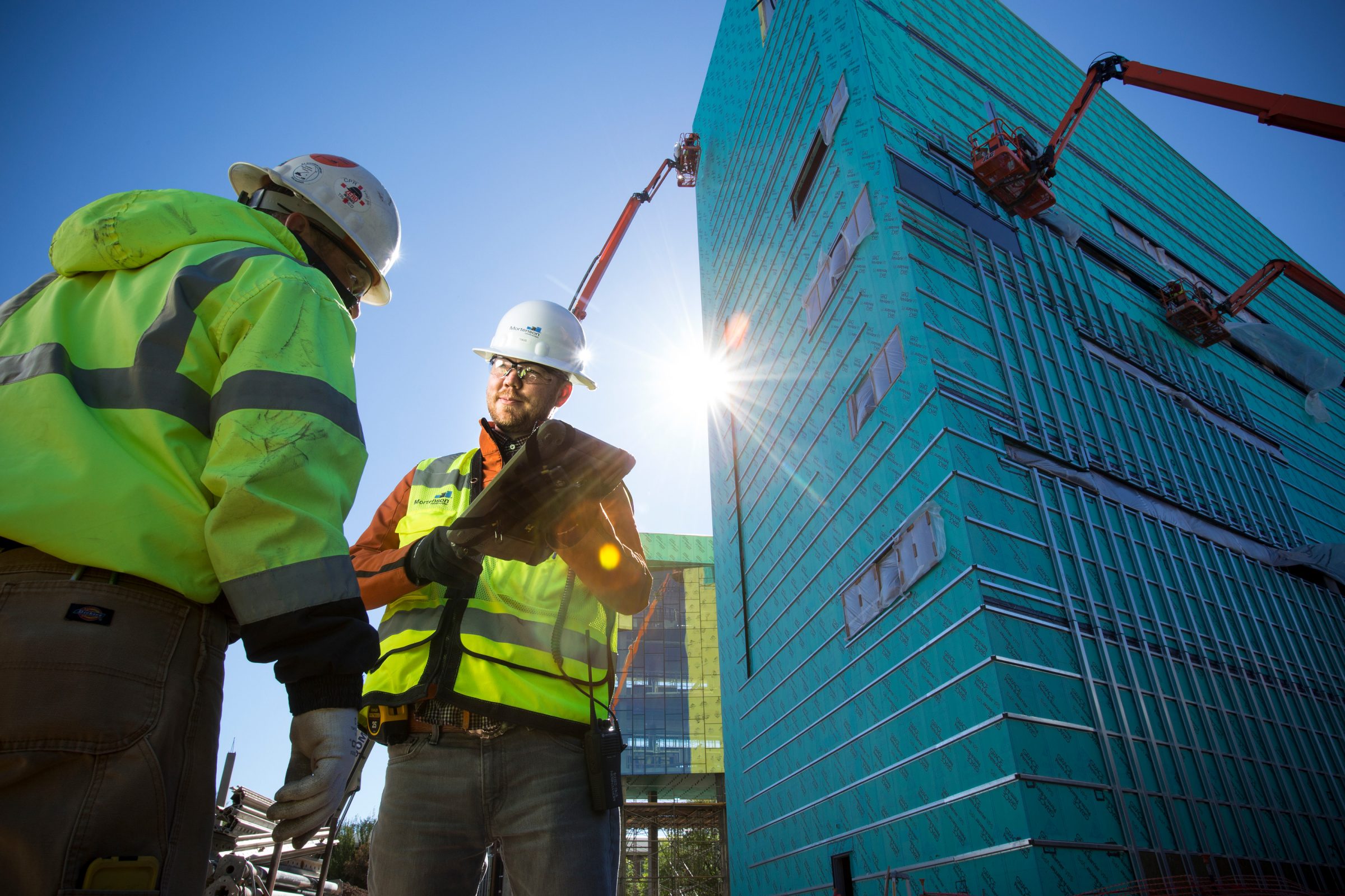Two contractors looking at a punch list with a construction project in the background.