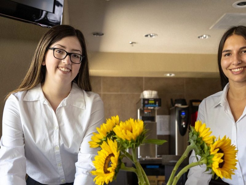 Two students setting a table with flowers.