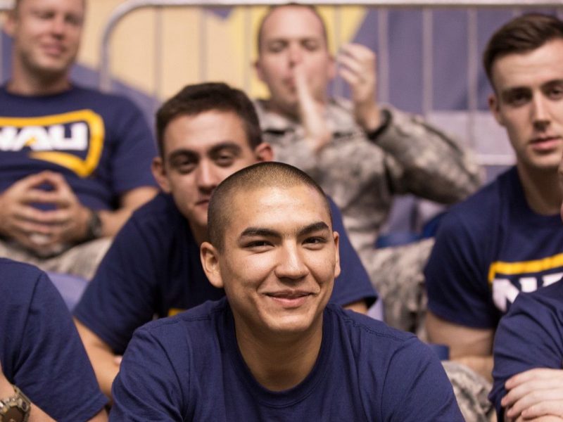 N A U military sit in the stands during a football game.