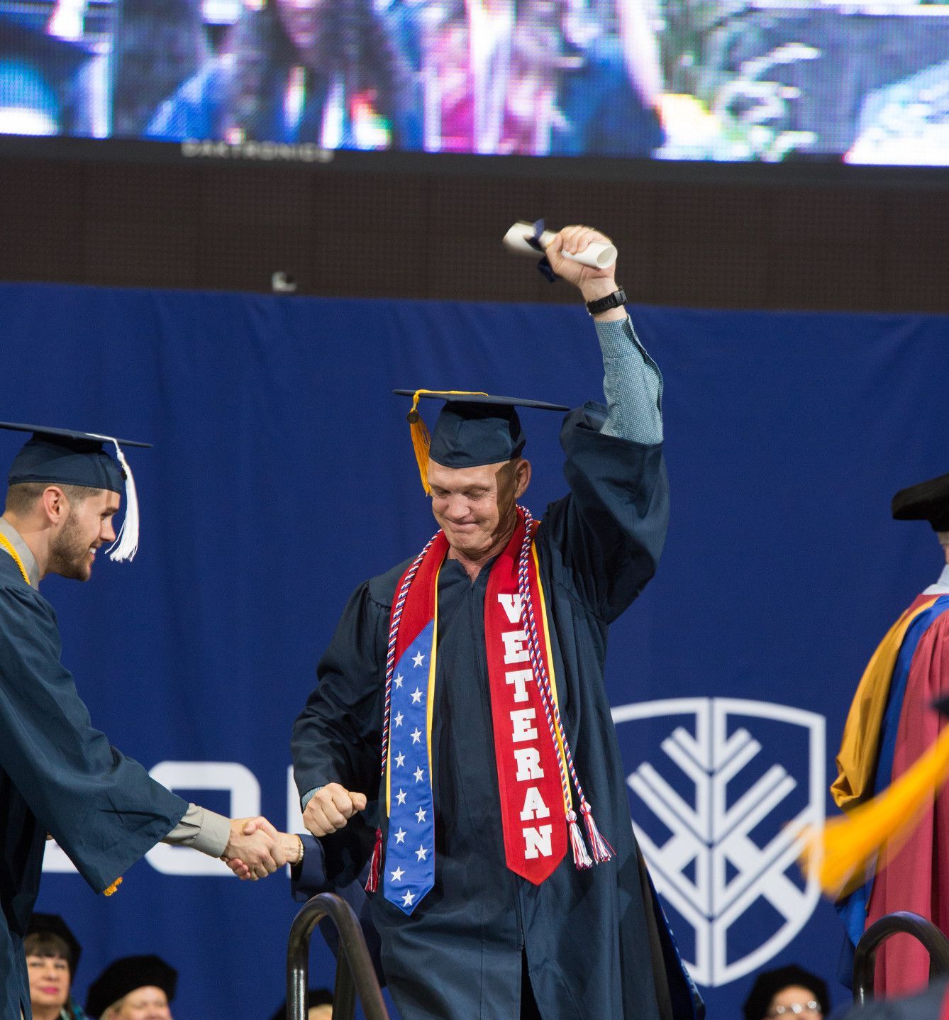 An N A U veteran graduates and holds his arm up in victory.