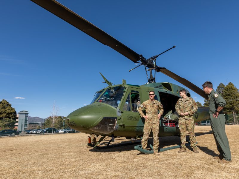 N A U military and veterans standing and talking next to a helicopter.