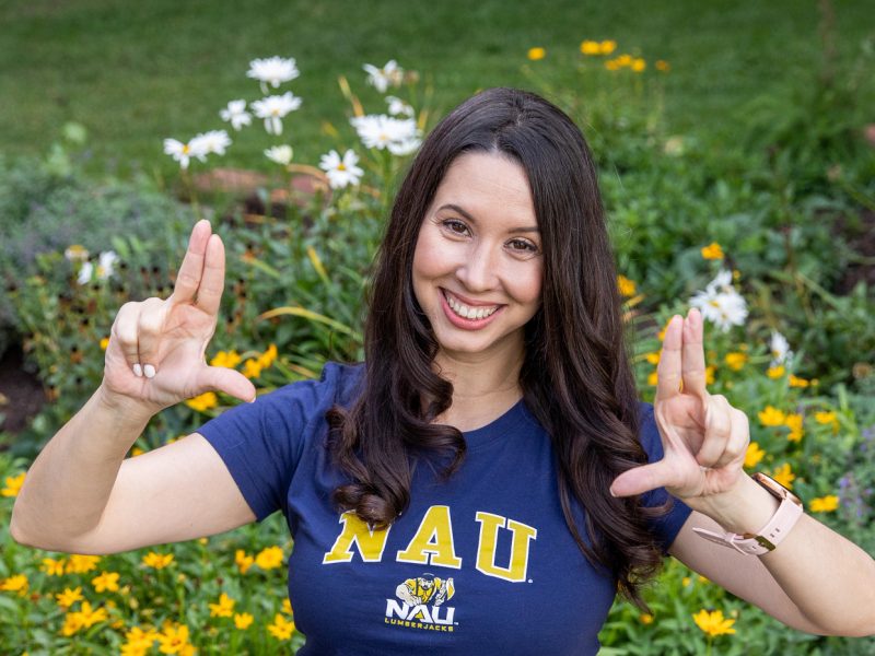 A student giving the "jacks up" hand sign while in front of some flowers.