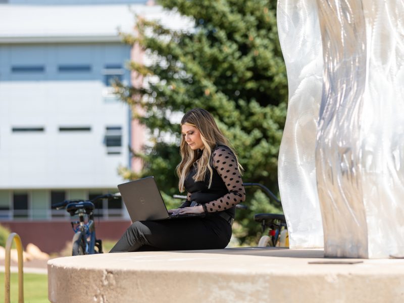Student works outside on her laptop.