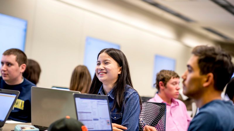 Smiling student sitting behind a laptop computer.
