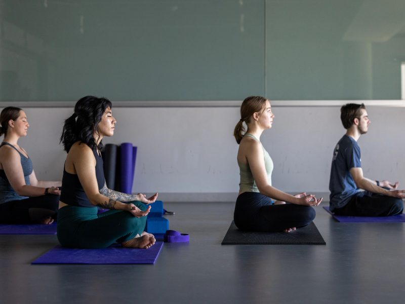 Four student sitting in an upright yoga pose facing the right.