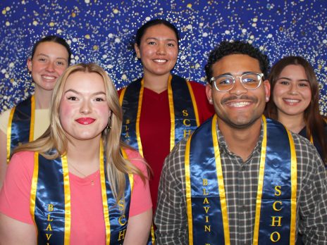 Five students smile at the camera wearing graduation stoles
