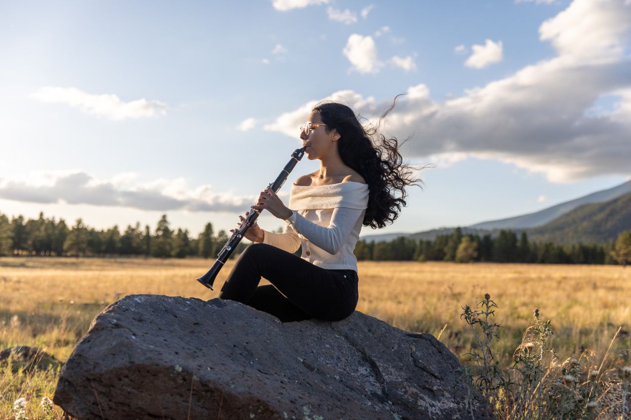 A person sitting on a rock playing a wind instrument.