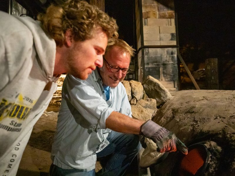 A professor and student looking into a kiln.