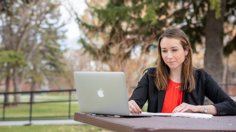 A student studying on their laptop at a table outside.
