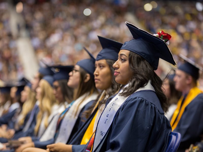 Students dressed in regalia sit in commencement.