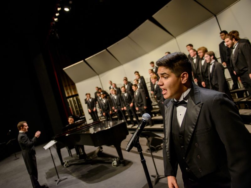 Students performing in suits on stage.