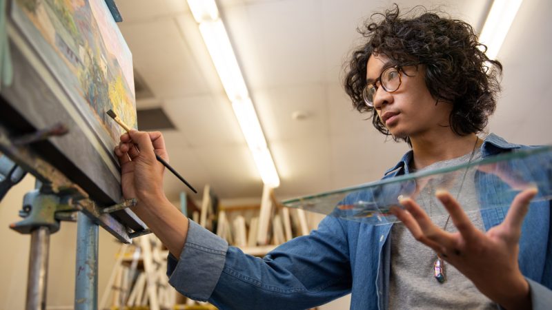 N A U art student Tripp Herrera paints on a canvas.