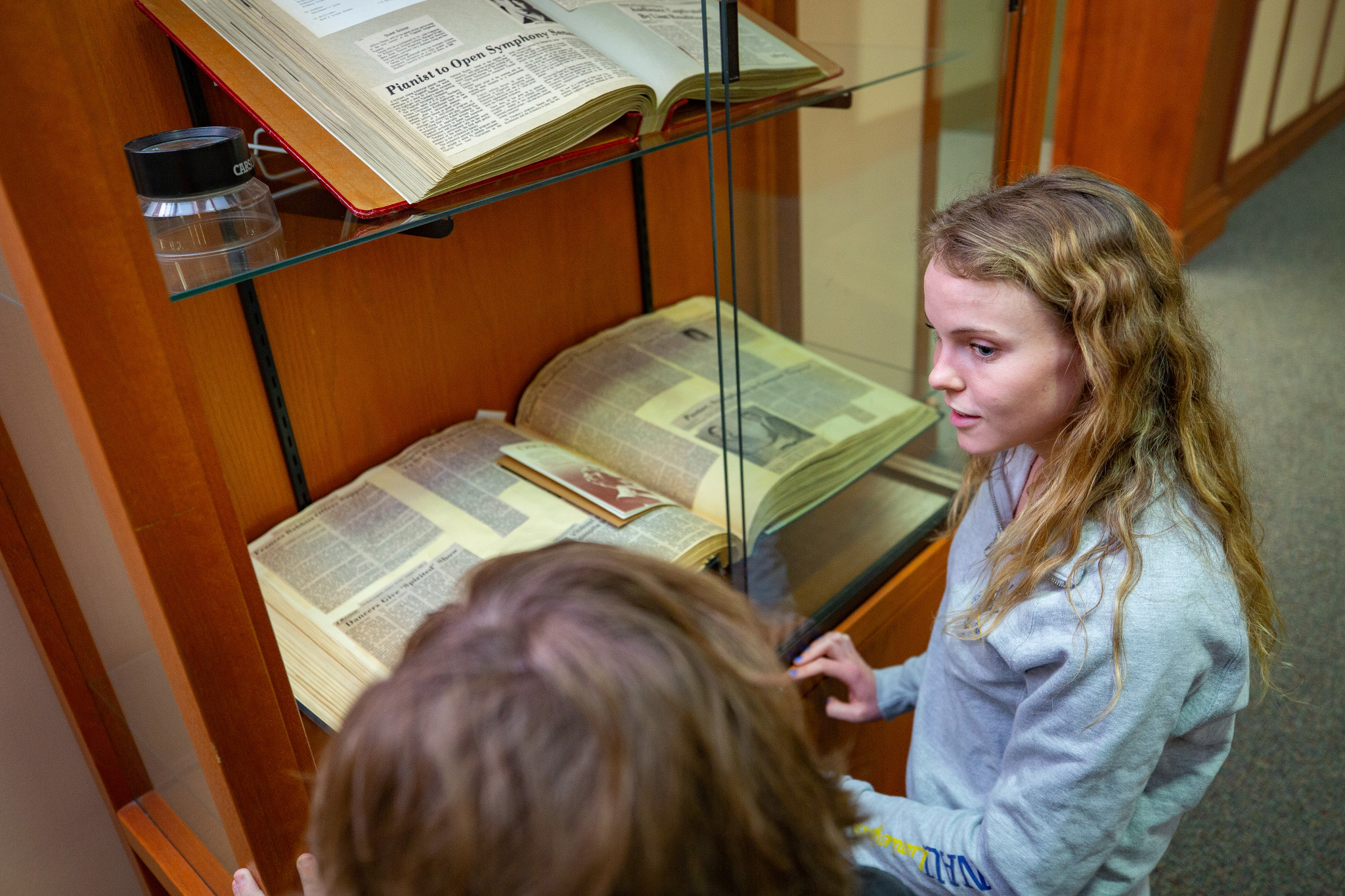 Students read historic textbook in glass display.