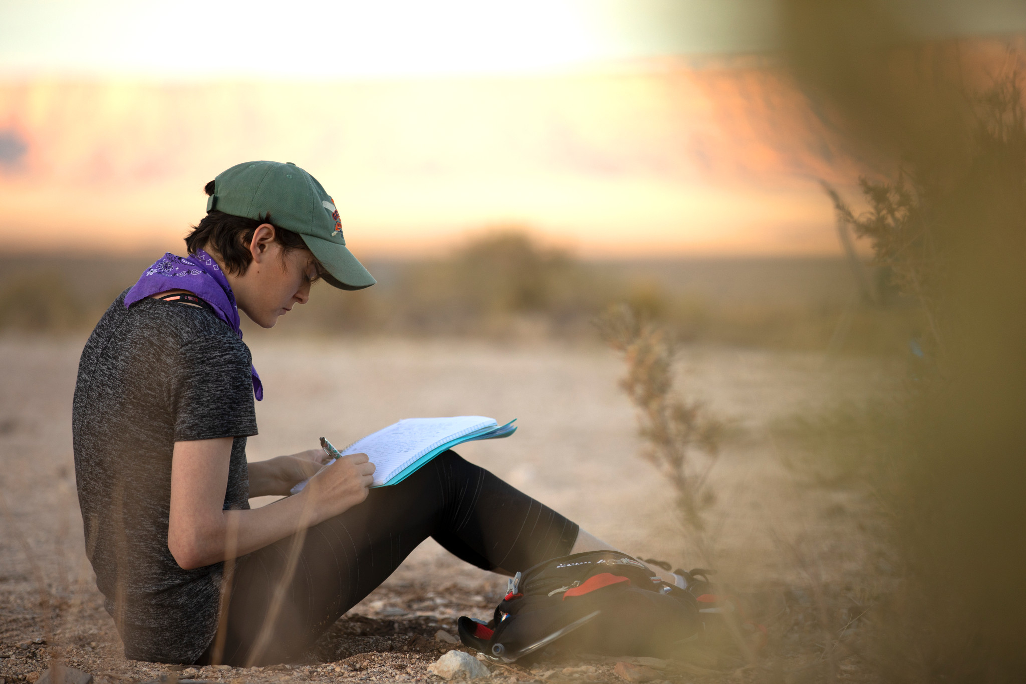 Student writes in a journal while sitting on the desert ground.