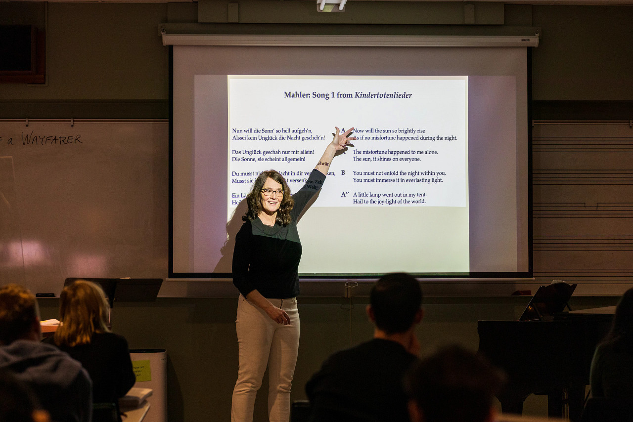 Person presenting to class in front of projected screen with look of interest and engagement.