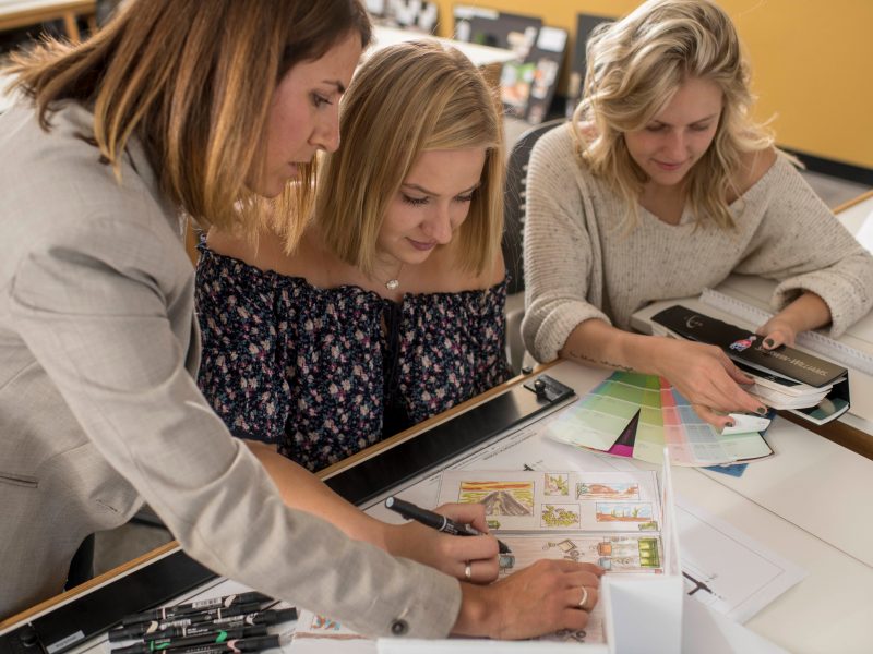 Three people looking at pallet boards and room layouts as they work on an interior design project.