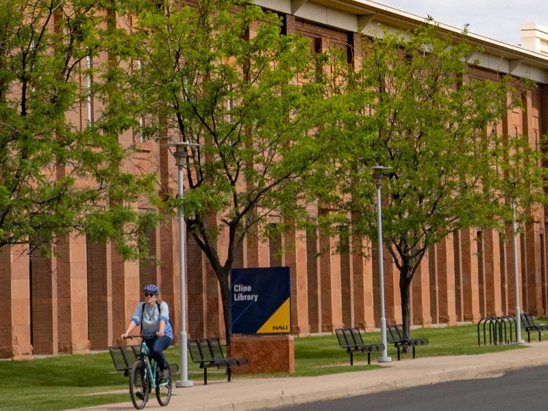 Exterior image of Cline Library at N A U with a student riding their bike.