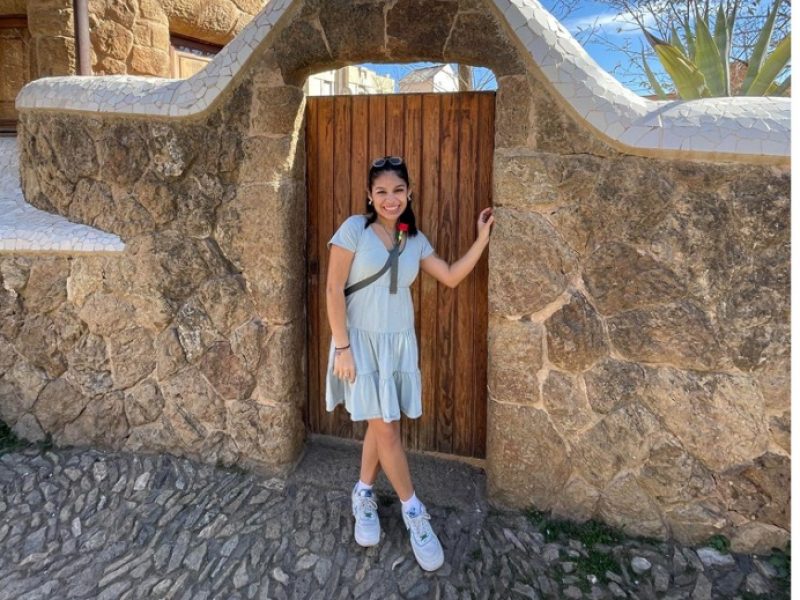 Ana standing in front of a gate in a stone wall in Europe.