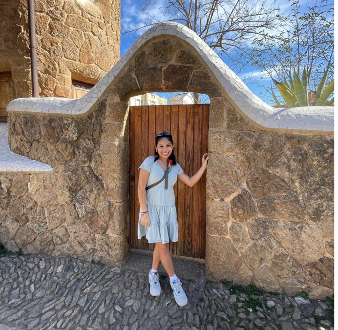 Ana standing in front of a gate in a stone wall in Europe.