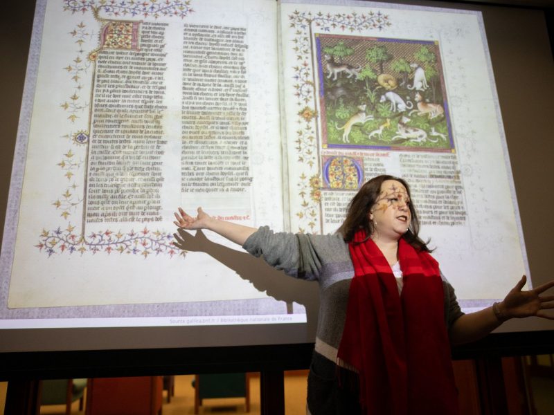 Teacher wearing red scarf presenting a powerpoint on medieval text.