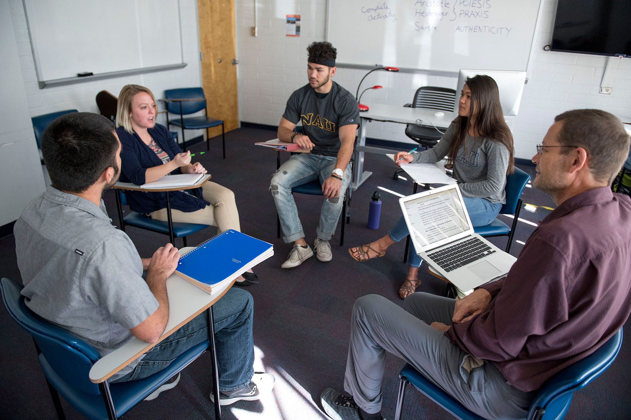 A group of students and professors sitting in desks in a circle talking to each other.