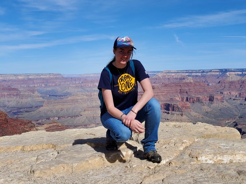 Kaylen Wilson kneeling down and smiling at the edge of the Grand Canyon.