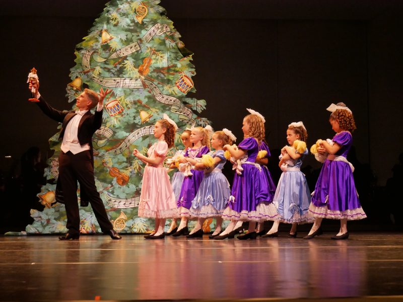 An adult leading children in dresses holding teddy bears in a performance.