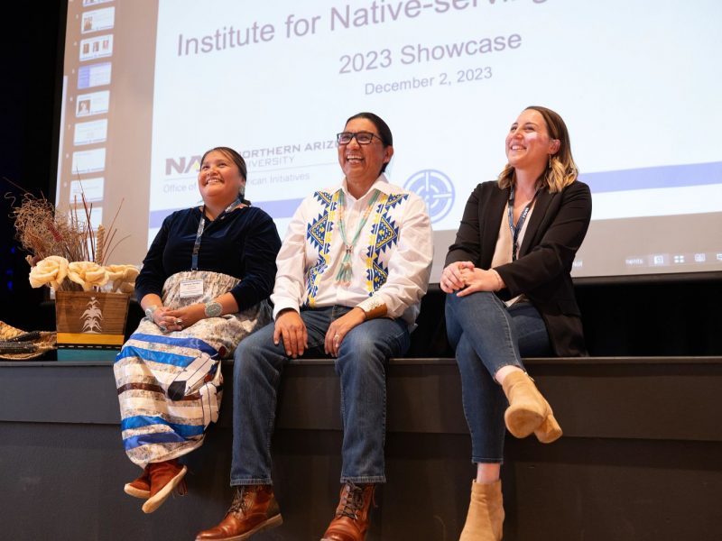 Three people sitting on the stage in front of a projector screen.