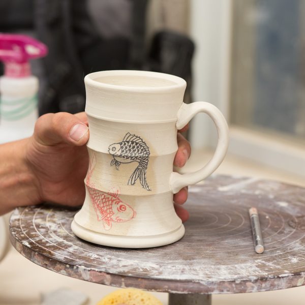 A hand holding a ceramic mug on a sculpting plate.
