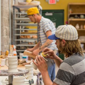 Students in a ceramics class shaping mugs.