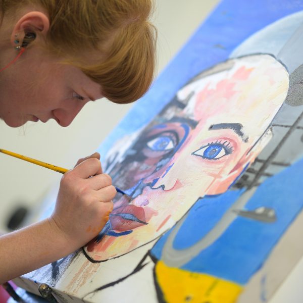 Student with headphones in working on a painting.