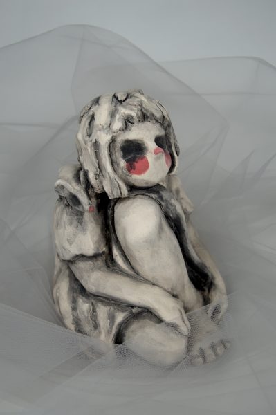 Sculpture of a girl with hollowed out eyes resting her head on her knee.