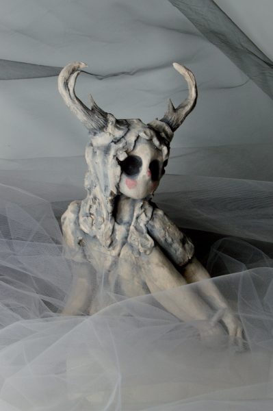Humanoid sculpture with hollow eyes and antler sitting down.