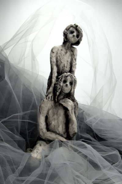 Two sculptures of girls with hollow eyes draped in white linen.