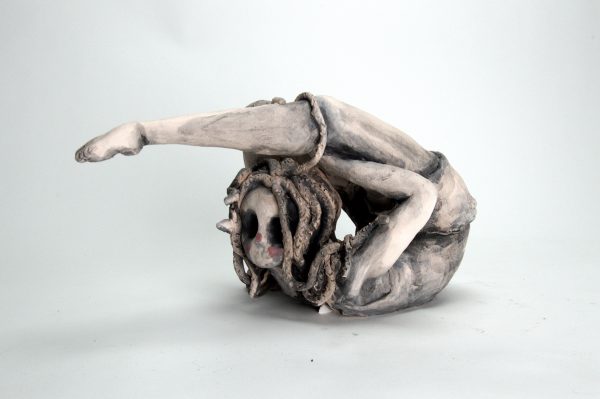 A medusa sculpture with hollow eyes in an acrobatic pose.
