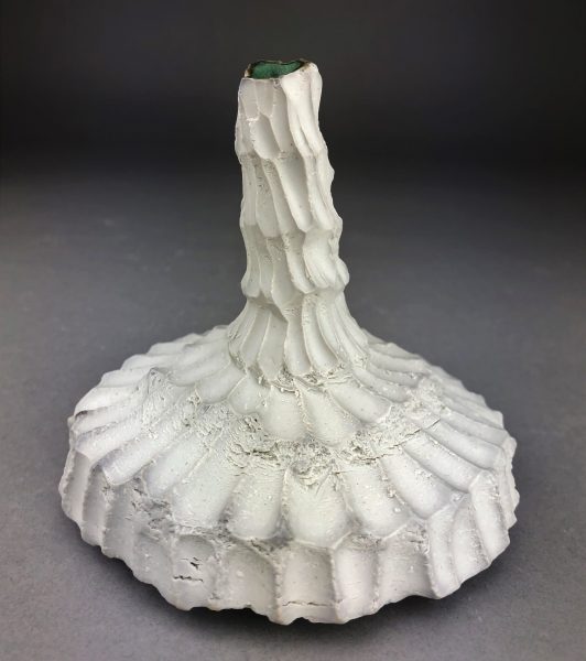 A white, scaled, ceramic vase-like sculpture called "Flakes."